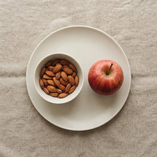 About 24 almonds in a small bowl on a plate, with a whole apple beside it for size
